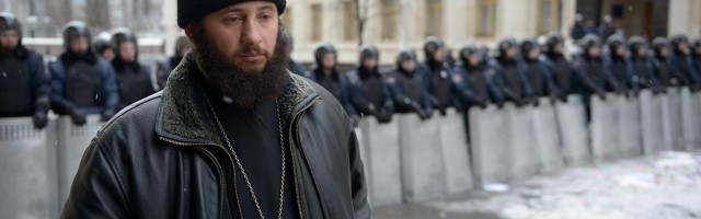Un cura -no sabemos si católico bizantino u ortodoxo- reza en silencio mientras se pasea interponiéndose entre manifestantes y policías
