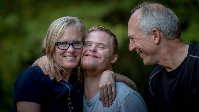 Un chico Down abraza sonriendo a sus padres.