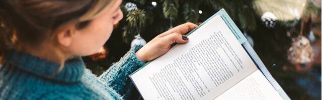 Una mujer lee un libro entre adornos navideños, foto de Red Charlie en Unsplash