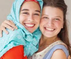 Dos chicas jóvenes se abrazan sonrientes, una de ellas con la cabeza cubierta con un velo musulmán.