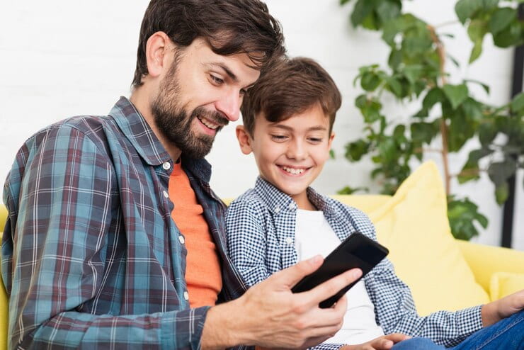 Un padre y su hijo se ríen juntos con un teléfono móvil