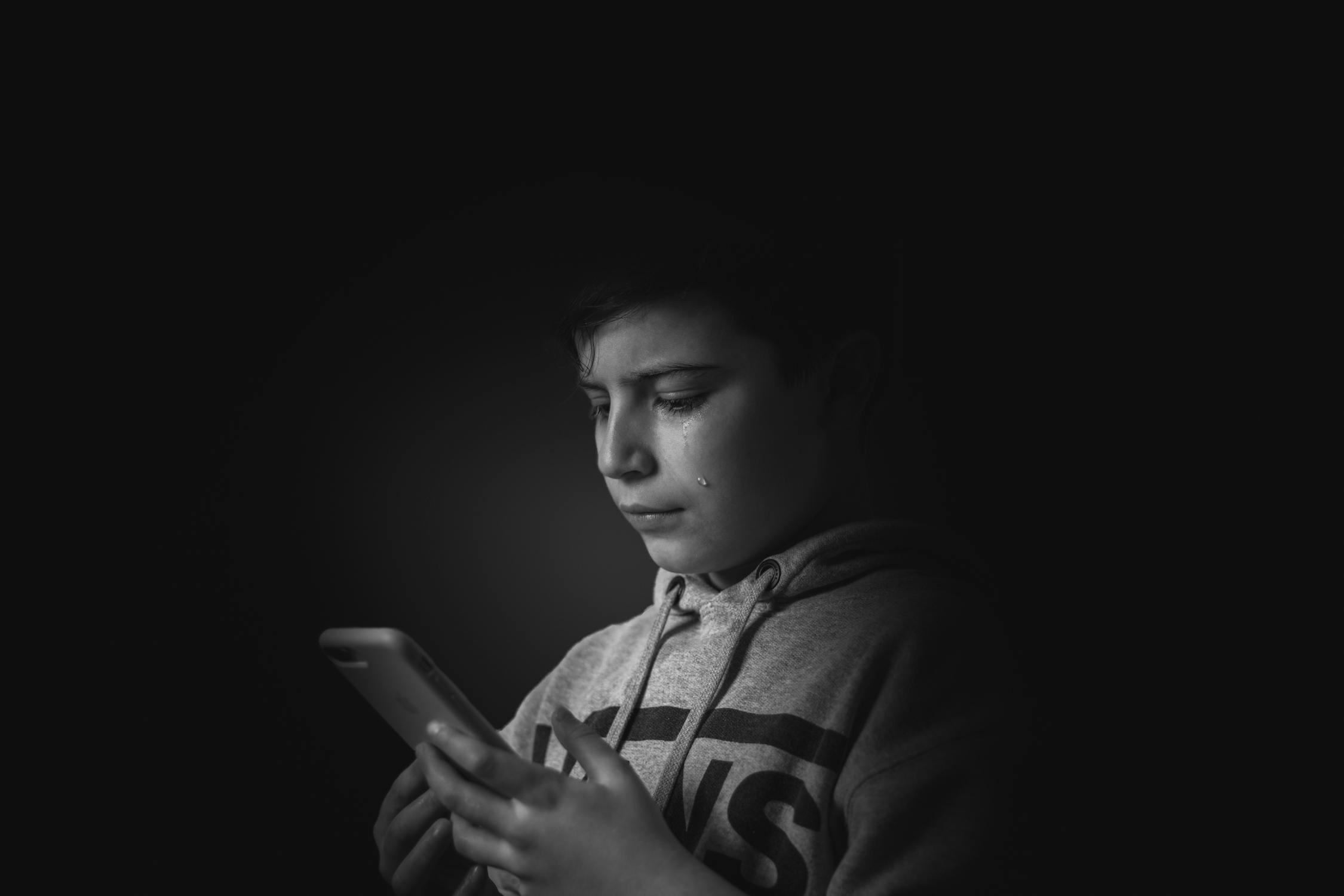 Un niño mira a su móvil, llorando.