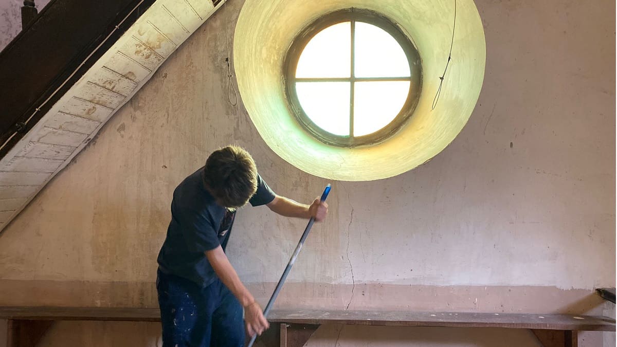 Un joven barre mirando al suelo, bajo un luminoso ventanal redondo