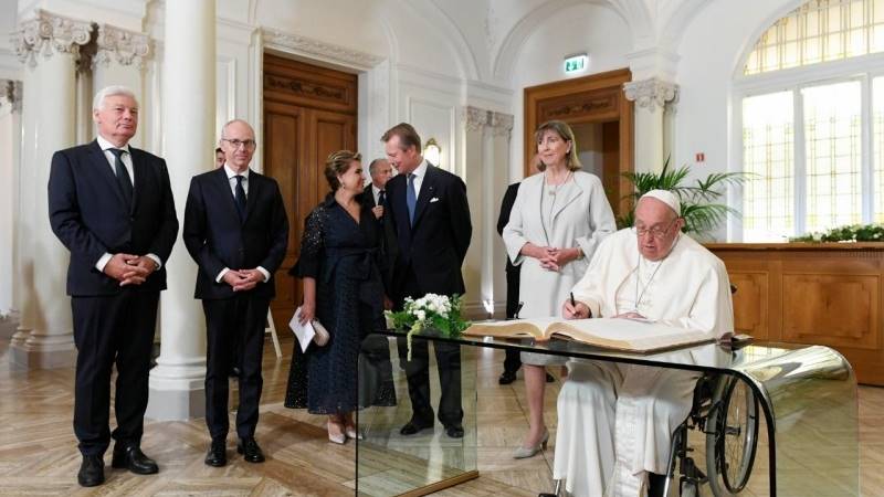 Francisco firma en el Libro de Honor del Palacio del Gran Duque de Luxemburgo, Enrique, quien conversa en el centro de la imagen. Foto: Vatican Media.