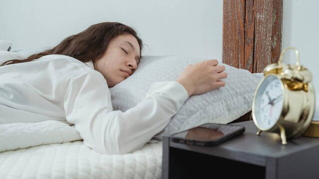 Joven mujer durmiendo junto al despertador.