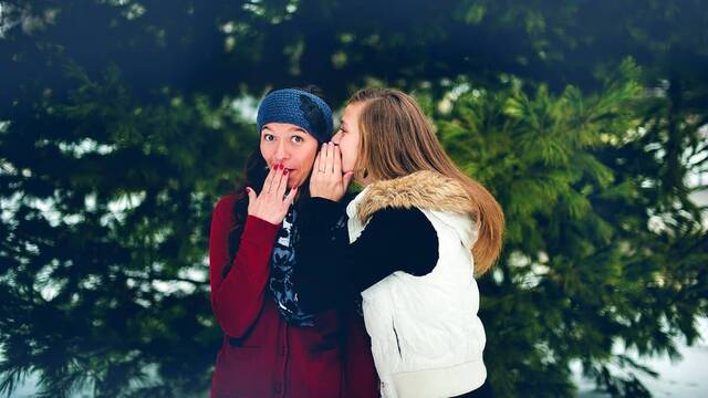 Dos jóvenes se dicen algo al oído en un bosque nevado.