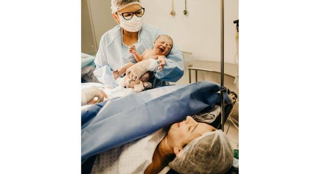 Mujer que acaba de dar a luz mira al hijo que le enseña la enfermera.
