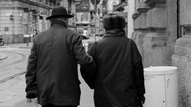 Un matrimonio anciano camina del brazo por la calle.