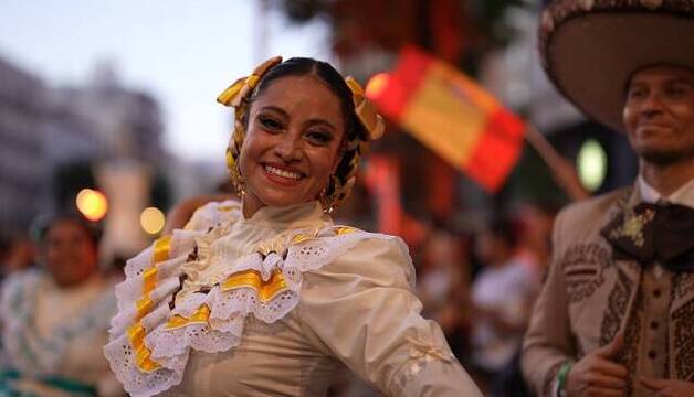 Una chica mexicana con traje típico baila, con bandera de España