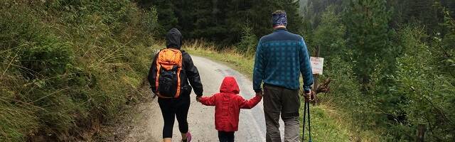 Padre, madre y niño pequeño caminan con lluvia cuesta arriba en montaña