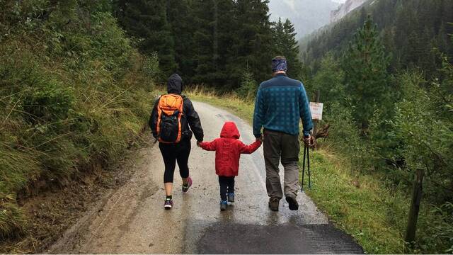 Padre, madre y niño pequeño caminan con lluvia cuesta arriba en montaña
