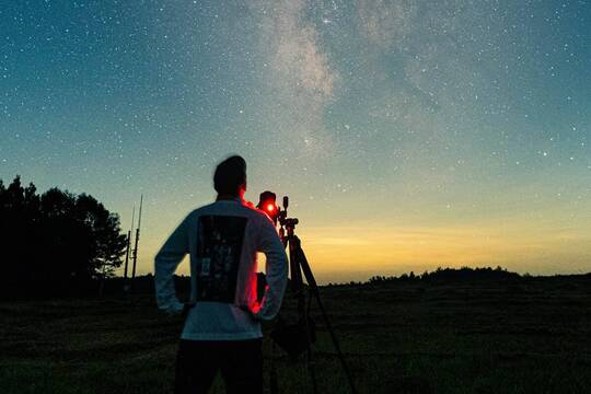 Un hombre con telescopio en el campo mira estrellas, foto de Kazuend en Unsplash