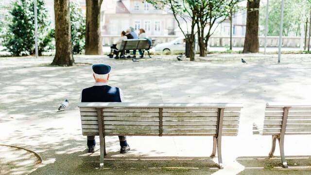 Un anciano sentado solo en un banco de un parque.