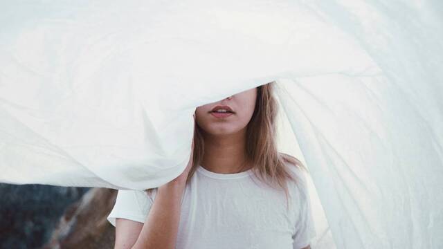 Joven mujer oculta su rostro con una sábana.