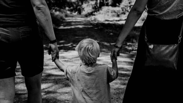 Un niño camina de la mano de sus padres.