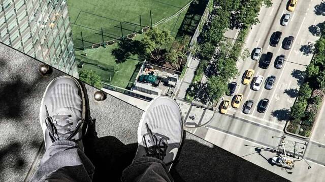 Pies de una persona asomada al abismo desde lo alto de un edificio.