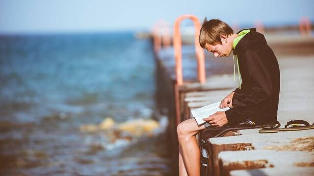 Joven leyendo sentado en el muelle, junto al mar.