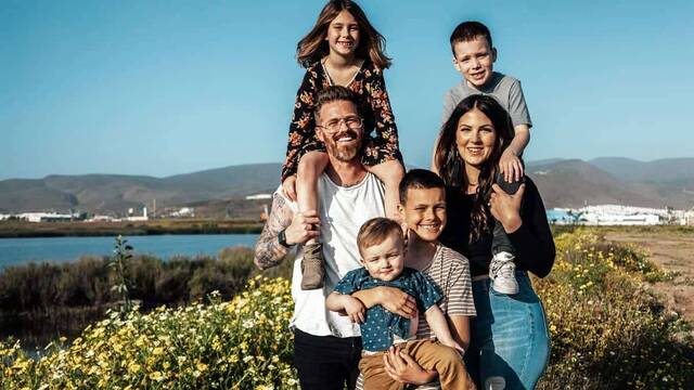 Familia con cuatro hijos sonríen a cámara ante el paisaje.