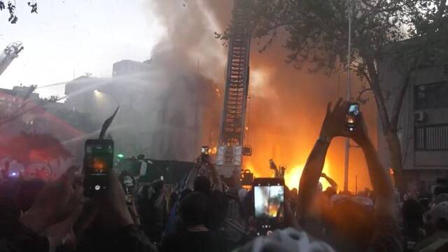 Los manifestantes de extrema izquierda celebran la caída de la torre de la iglesia de la Asunción, en Santiago, que previamente habían quemado.