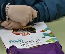 Una niña con un libro de Religión en su pupitre.