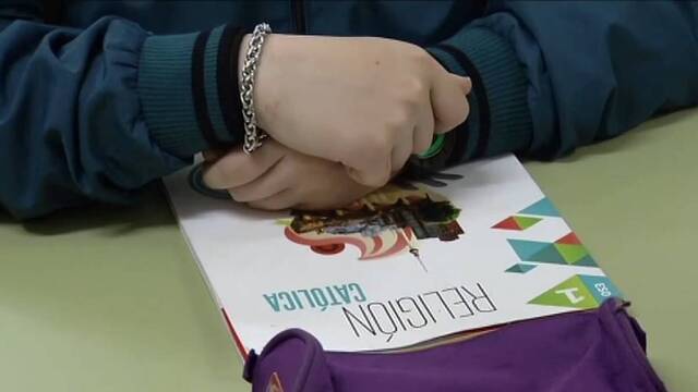 Una niña con un libro de Religión en su pupitre.