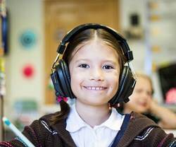 Niña en un aula con los auriculares puestos.