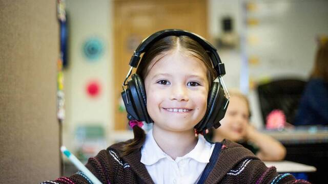 Niña en un aula con los auriculares puestos.