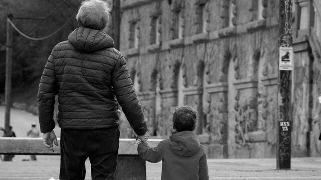 Un abuelo con su nieto, de espaldas, contemplan un viejo edificio.