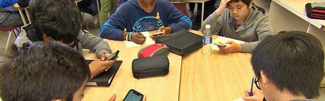 Niños estudiando en el colegio con el móvil en la mano.