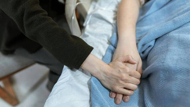 Un visitante toma de la mano a un paciente en la cama del hospital.