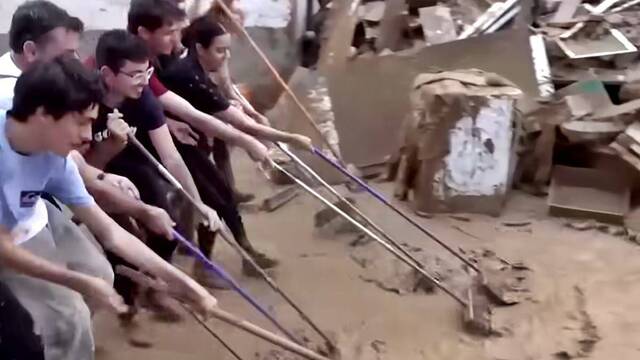 Voluntarios cooperando con escobas en la limpieza del barro en Valencia.