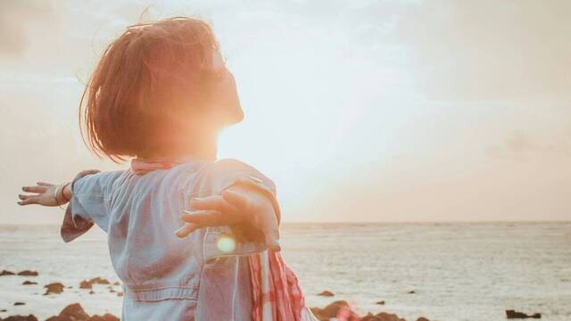 Una mujer abre los brazos ante el sol del amanecer, en la playa.