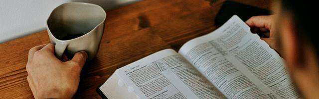 Hombre leyendo la Biblia mientras toma un café.