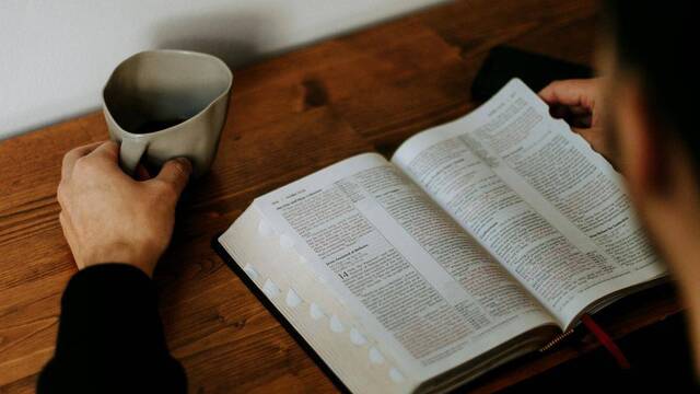 Hombre leyendo la Biblia mientras toma un café.