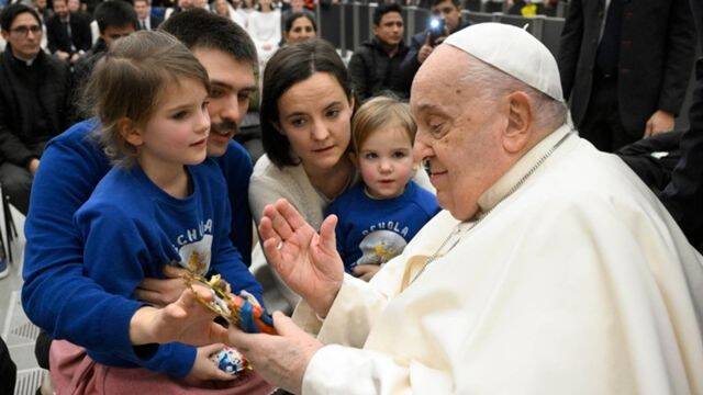 Francisco bendice una imagen del Niño Jesús al ser saludado por una familia presente en la audiencia. Foto: Vatican Media.