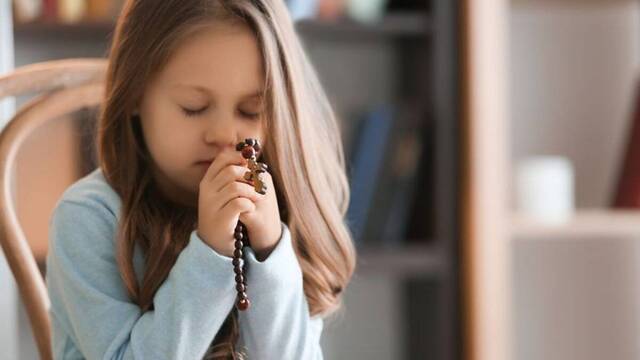 Una niña rezando el rosario.